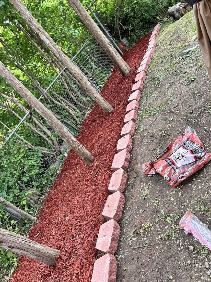 Fresh mulch bed with stone edging along a fence